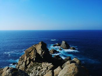 Rock formation in sea against clear blue sky