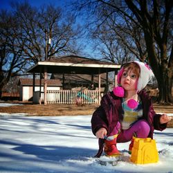 Full length of cute girl crouching on snow covered field in park