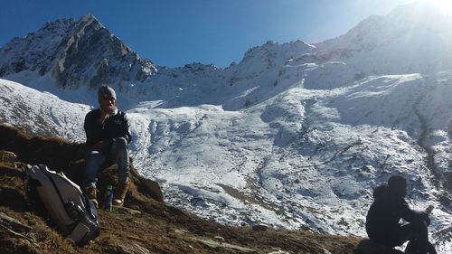 Man sitting on snowcapped mountain against sky