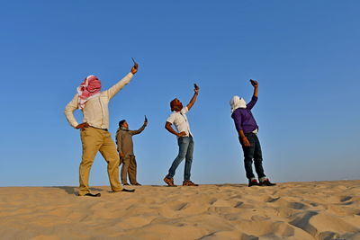 Men with covered face taking selfie while standing on sand at beach