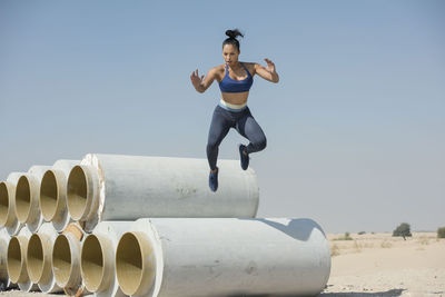 Woman jumping over pipe against sky