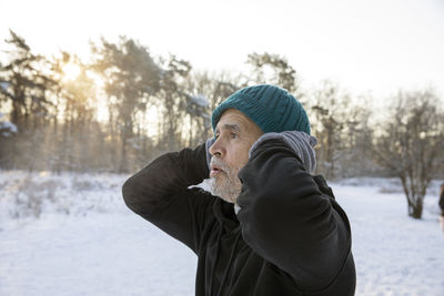 Senior man with hands behind head wearing knit hat during winter