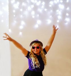 Cute girl with arms raised against illuminated wall at party