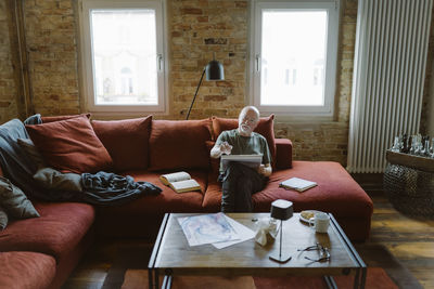 Senior man doing painting while sitting on sofa in living room at home