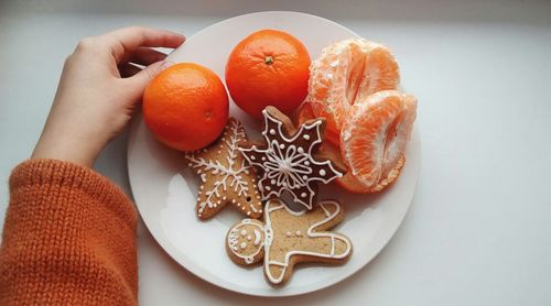 High angle view of hand holding gingerbread cookies and orange fruits in plate