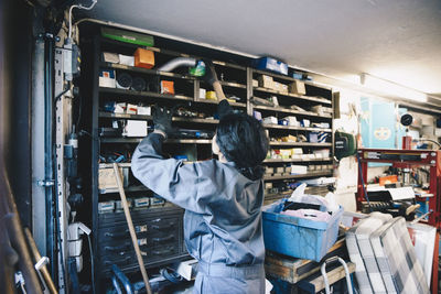 Female mechanic searching equipment on shelf at auto repair shop