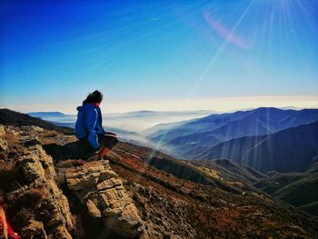 Woman looking away while sitting on mountain against blue sky