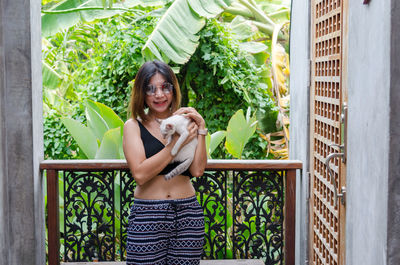 Portrait of smiling young woman holding cat at balcony