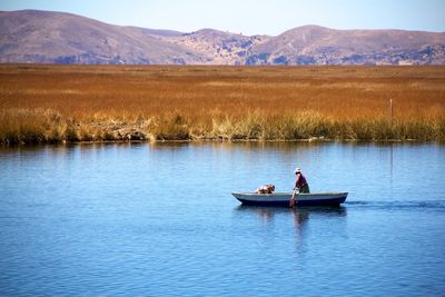 People rowing boat in river against mountains