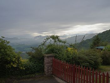 Fence by trees on mountain against sky