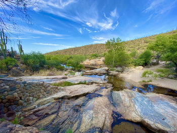 Stream flowing through rocks against blue sky