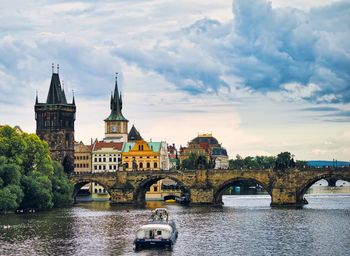 Bridge over river in city against cloudy sky