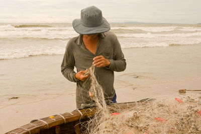 Man holding fishing net while standing at beach