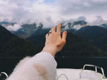 Cropped hand of woman against mountain range against sky