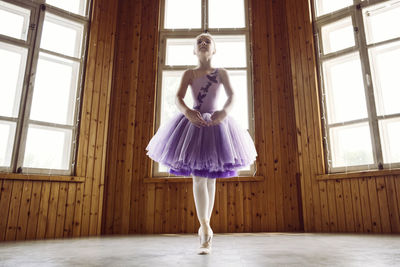 A portraits of a ballerina girl in a lilac dress posing in a room showing ballet poses