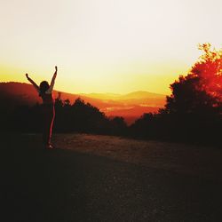 Silhouette of woman walking on landscape at sunset