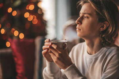 Portrait of candid authentic smiling handsome boy teenager using mobile phone at xmas home interior