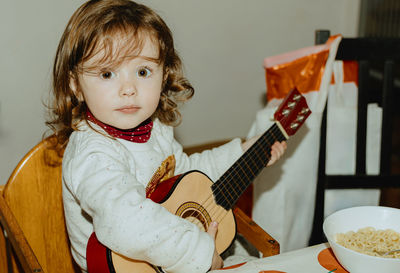 A little girl plays the guitar while sitting at the table.