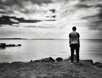 Rear view of teenage boy looking at sea against cloudy sky