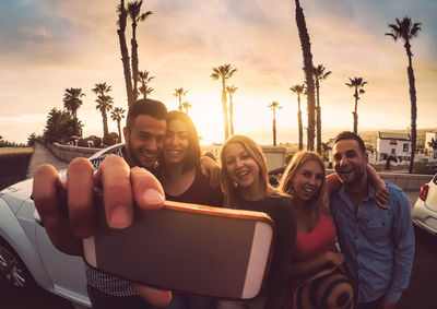 Happy friends posing for cellphone selfie in city during sunset