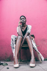 Young woman sitting against pink background