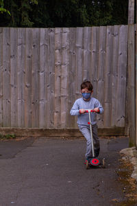 Full length of boy riding a scooter  against fence