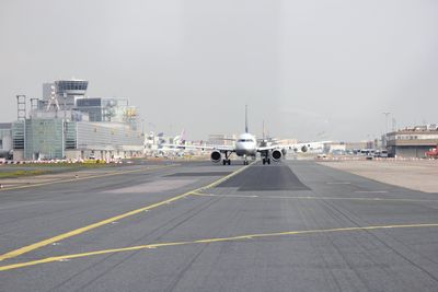 Airplane on airport runway against sky in city