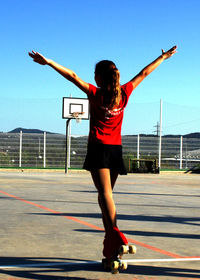 Rear view of girl with arms outstretched skating on sunny day