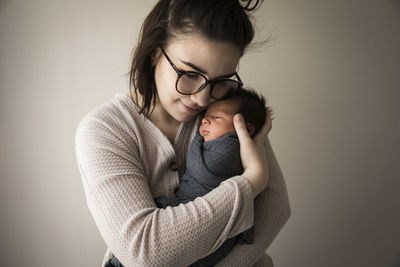 Modern millennial hipster mom snuggles swaddled newborn baby son