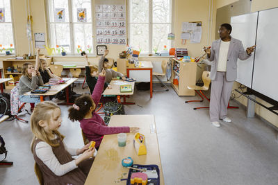 Teacher standing by whiteboard while asking questions to students in classroom