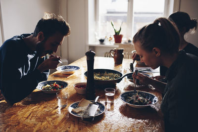 Side view of couple eating pasta with female friend at home