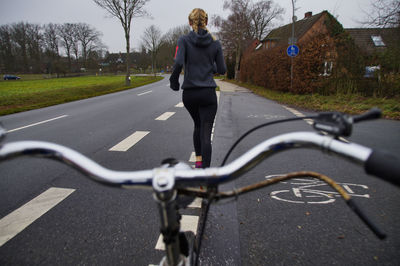 Close-up of bicycle handlebar with woman running in background on road