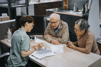 Female interior designer discussing over brochure with senior couple at desk in store