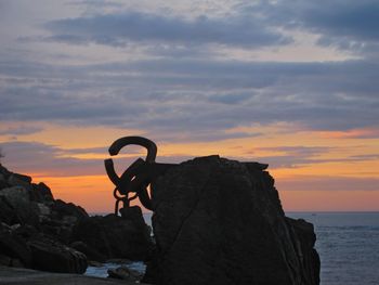 Silhouette man on rock by sea against sky during sunset