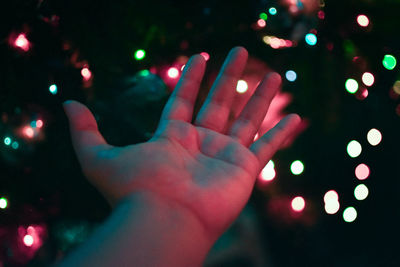 Cropped hand gesturing against illuminated christmas lights at night