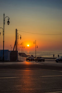 Cars on street by sea against sky during sunset