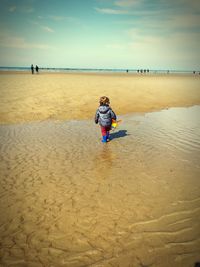Rear view of boy walking on beach against sky
