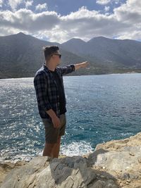 Young man standing on sea shore against mountains