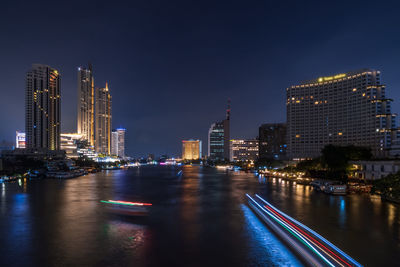 Illuminated buildings by river against sky at night