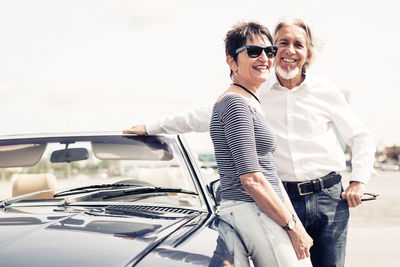 Happy friends standing on car against sky