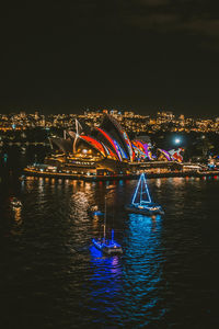 Illuminated city by river against sky at night