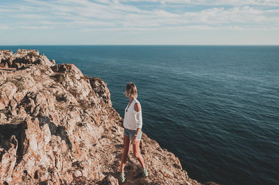 Rear view of man standing on rock by sea against sky