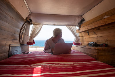 Teenager boy using laptop while lying on motor home against sea