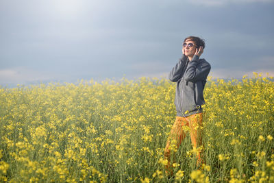 Mid adult woman listening music while standing on grassy field against cloudy sky