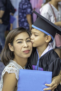 Portrait of smiling mother being kissed by son in graduation gown