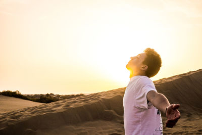 Boy standing on beach against sky during sunset