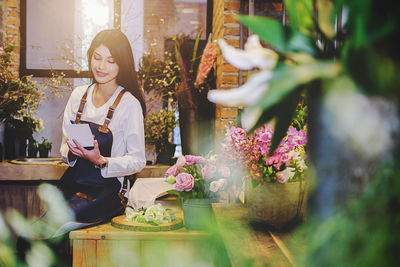 Woman writing in paper while sitting at flower shop