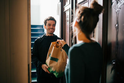 Smiling delivery man delivering bag to woman standing at doorway