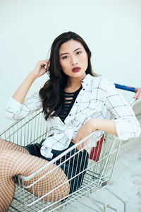Portrait of beautiful young woman sitting in shopping cart