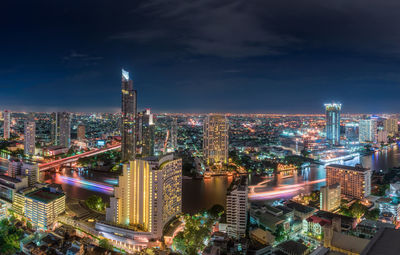 Illuminated buildings along chao phraya river in city against sky